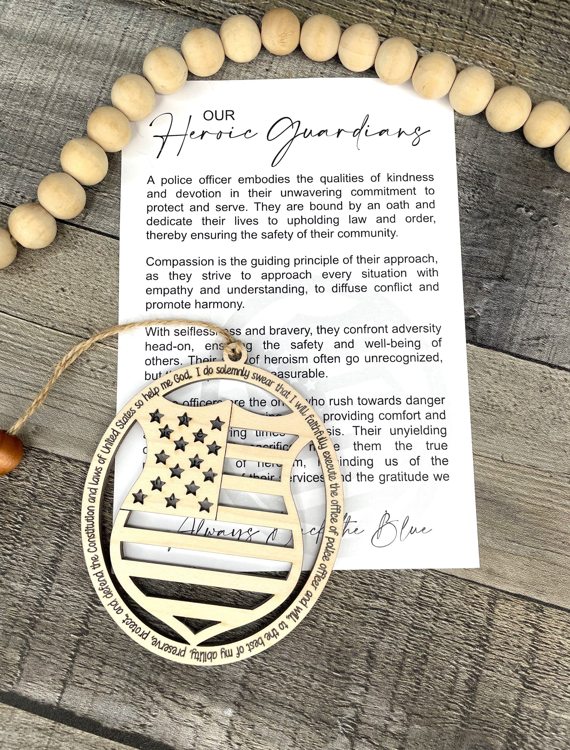 A printed card titled 'Our Heroic Guardians' with a quote about police officers, displayed on a rustic gray wood surface with wooden ornament that reflects a USA flag and badge. 