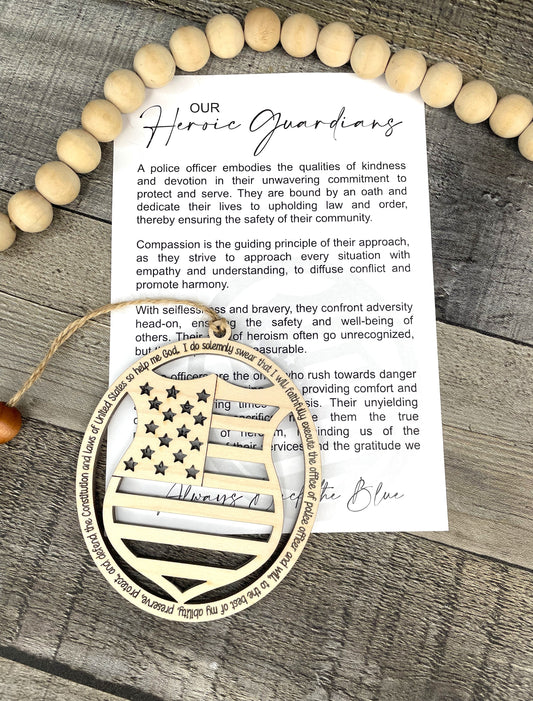 A printed card titled 'Our Heroic Guardians' with a quote about police officers, displayed on a rustic gray wood surface with wooden ornament that reflects a USA flag and badge. 