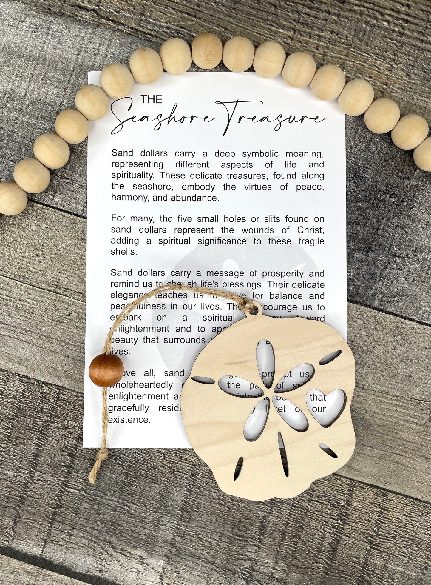 A flat-lay of a printed card titled 'The Shoreline Treasure' with sand dollar ornament arranged on a weathered wood surface.