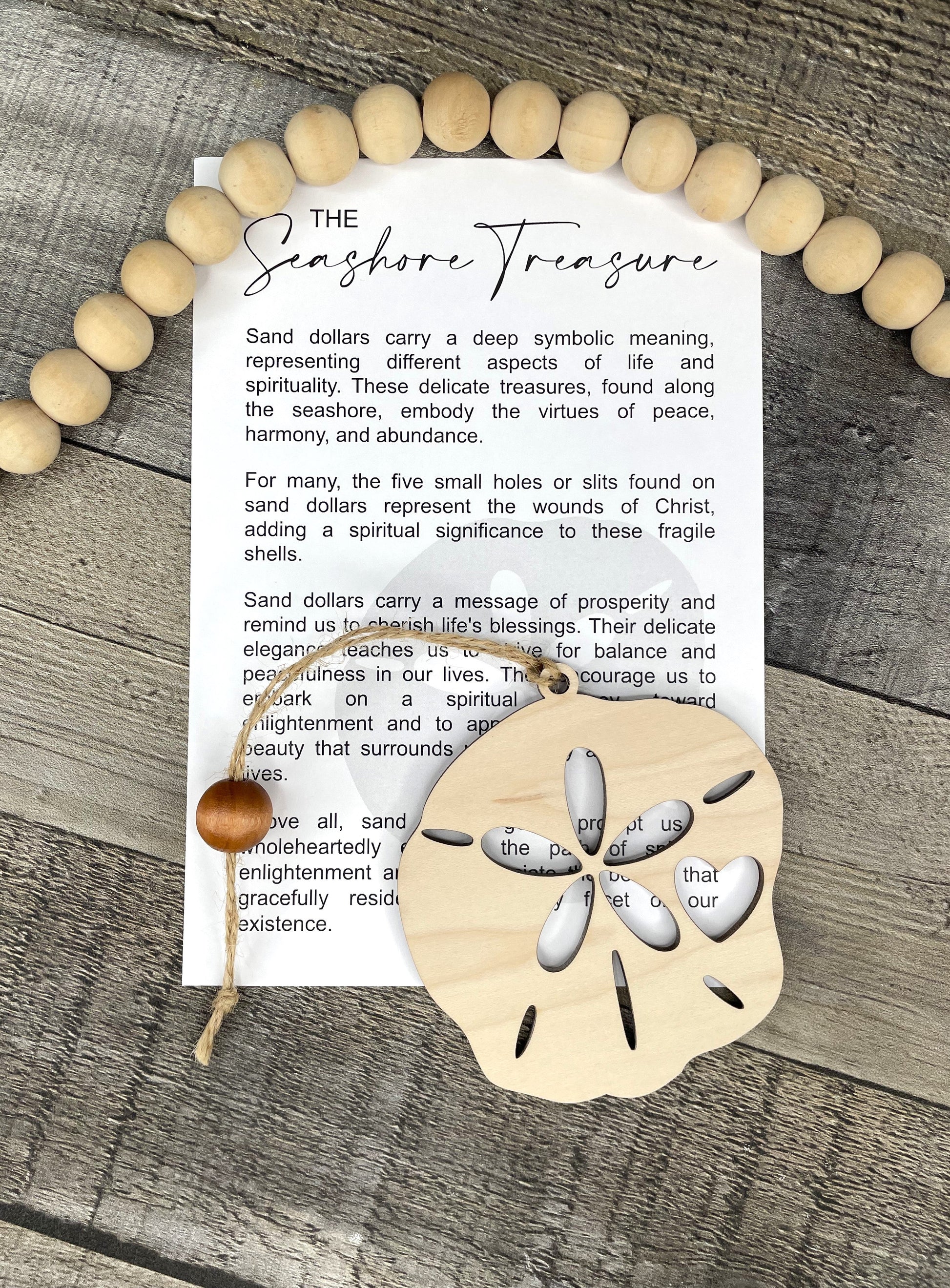 A flat-lay of a printed card titled 'The Shoreline Treasure' with sand dollar ornament arranged on a weathered wood surface.